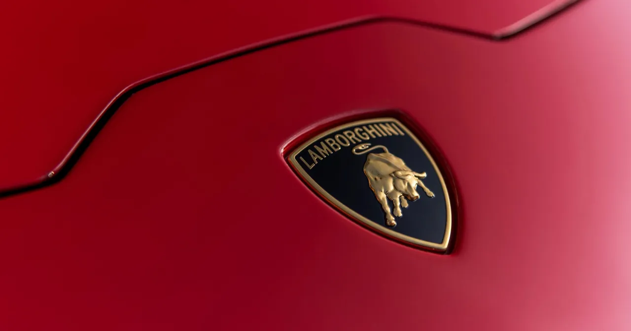 Złote logo byka na czerwonym tle samochodu Lamborghini. To Ferruccio Lamborghini stworzył te luksusowe auta.