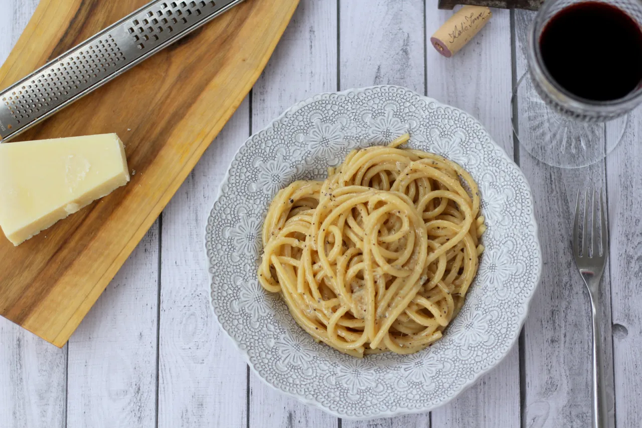 Pyszne spaghetti Cacio e Pepe na talerzu, obok kawałek sera, tarka i kieliszek czerwonego wina. Idealny przepis na szybki obiad.