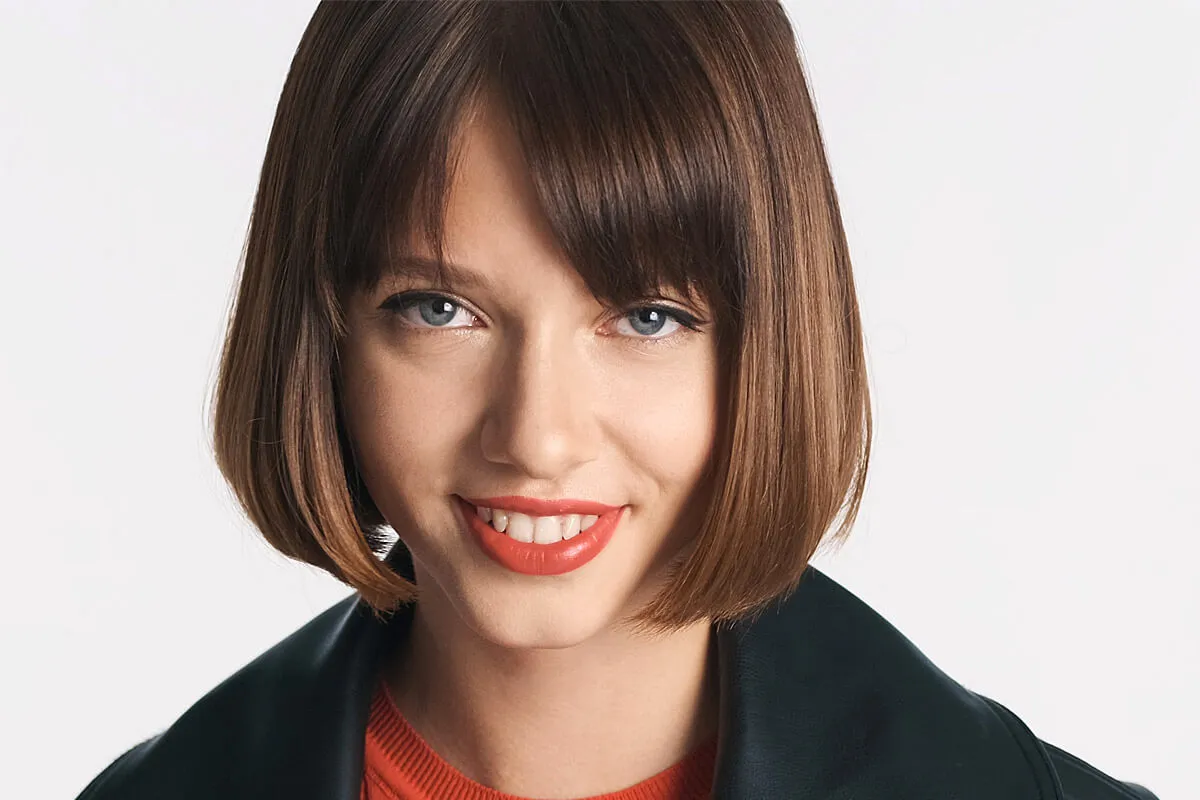 Kr&oacute;tkie, brązowe włosy z grzywką idealnie maskują wysokie czoło i zakola, tworząc stylową fryzurę damską.