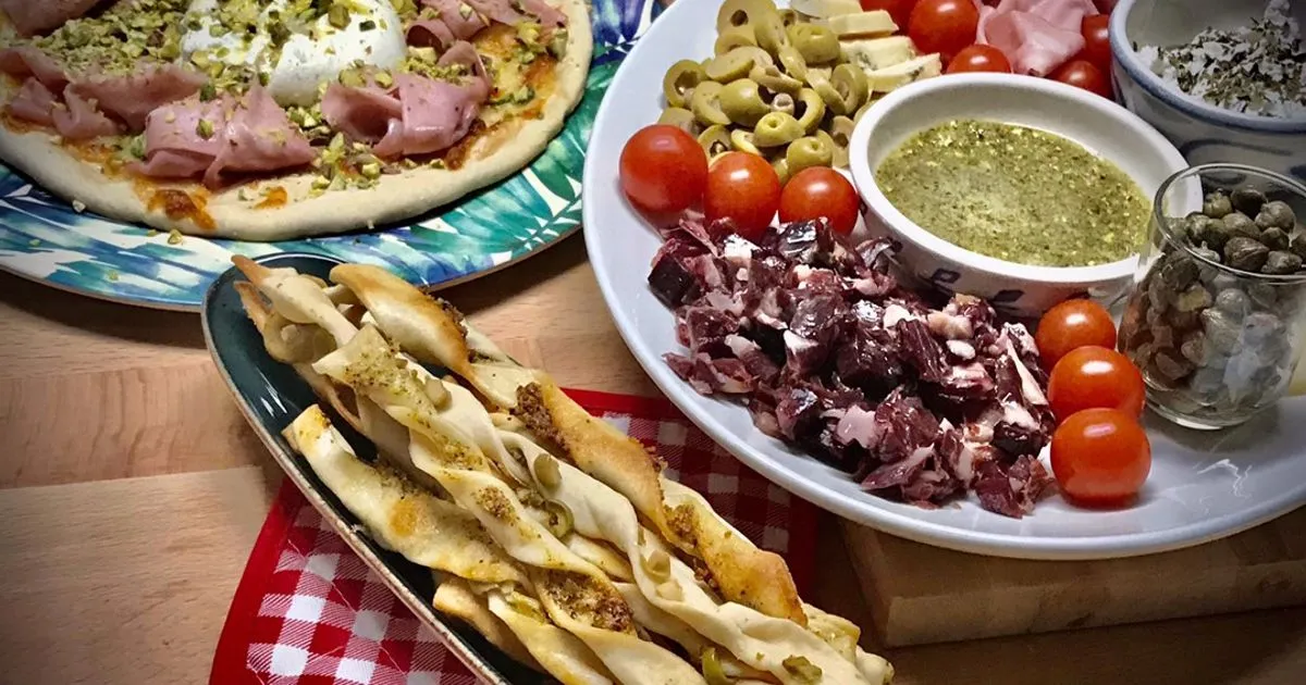 Mesa italiana con antipasti variados como burrata y porchetta junto a una pizza