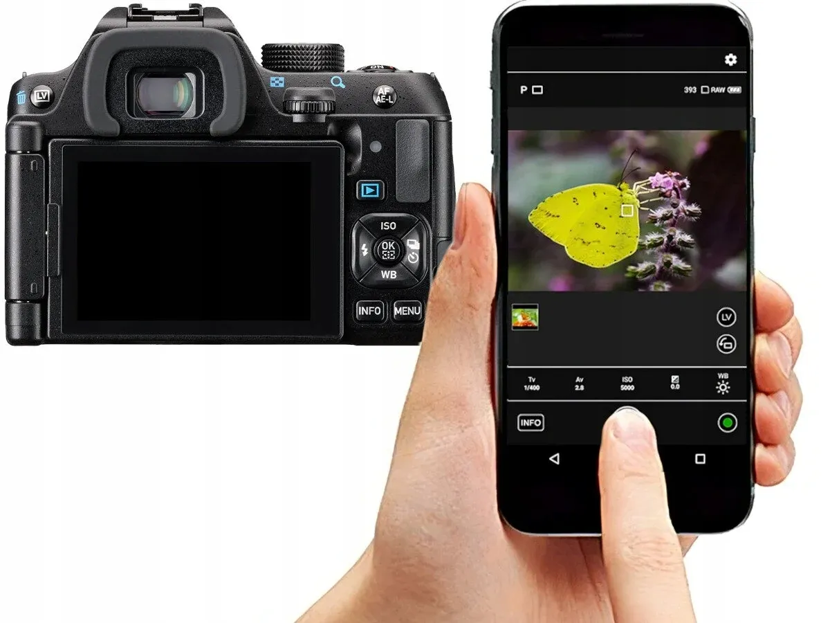 Tył lustrzanki Pentax KM obok smartfona sterującego aparatem. Na ekranie telefonu zdjęcie żółtego motyla.