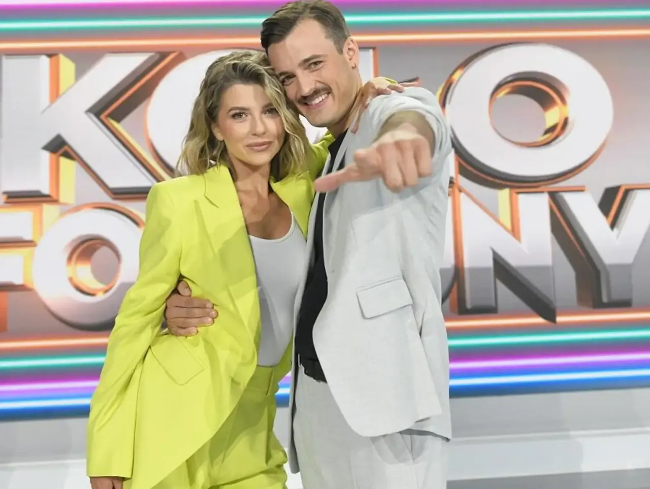 Para w neonowych barwach na tle logo 