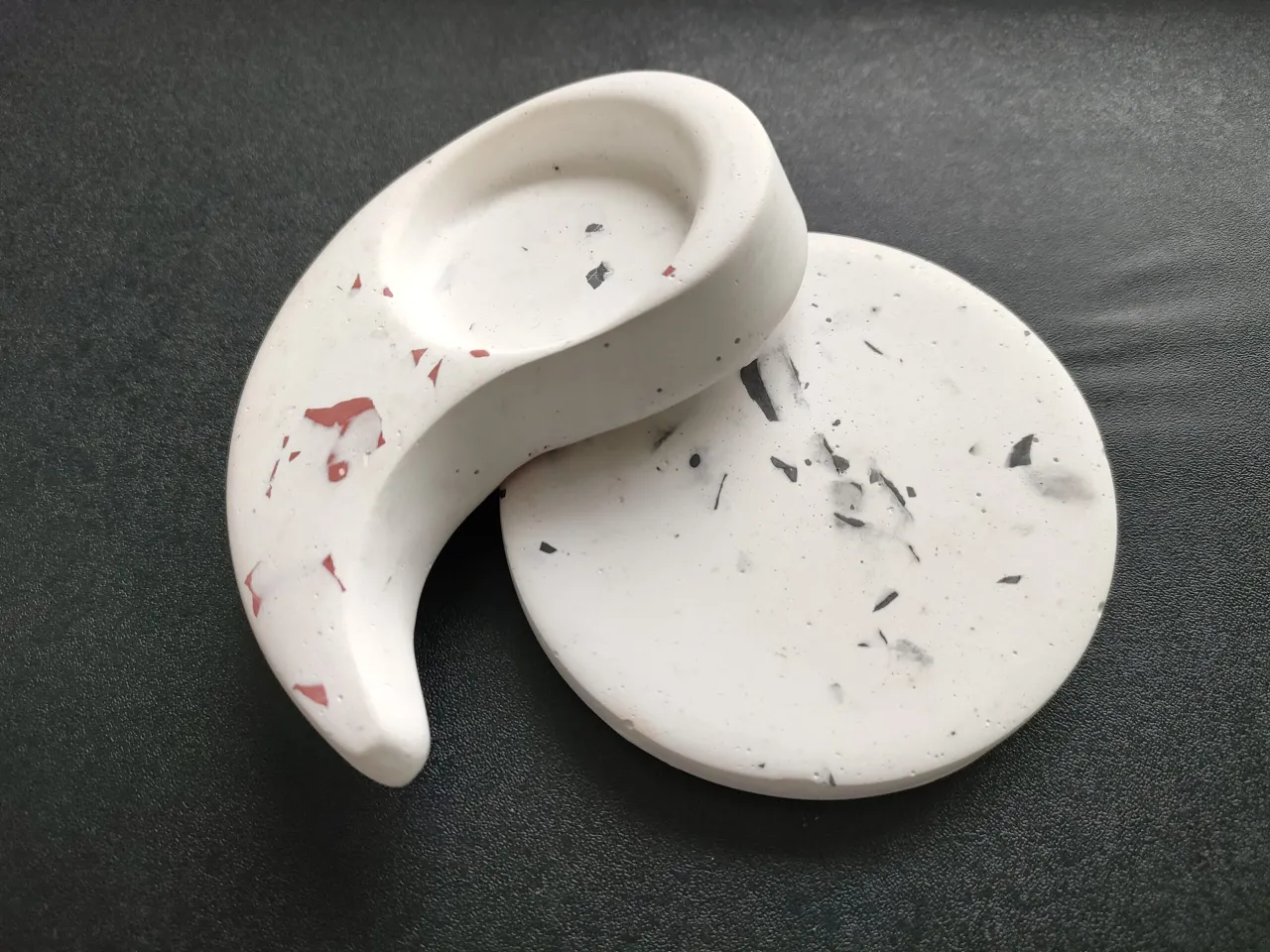 Gips polimerowy gdzie kupić? Dwa ozdobne elementy z gipsu polimerowego, jeden w kształcie półksiężyca, drugi okrągły, z czarnymi i czerwonymi wtrąceniami.