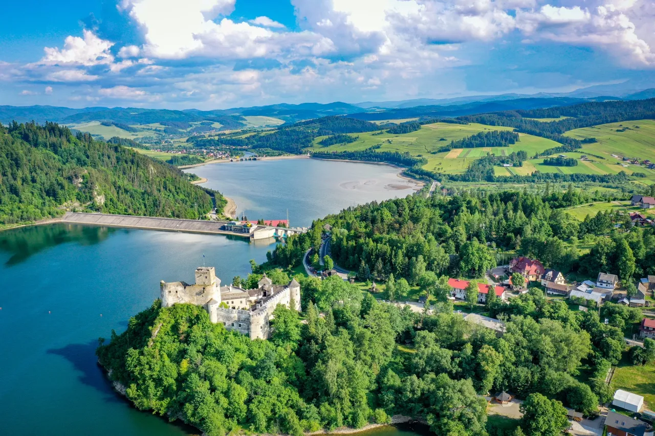 Zamek w Czorsztynie majestatycznie wznosi się nad jeziorem, otoczony zielonymi wzgórzami i lasami.