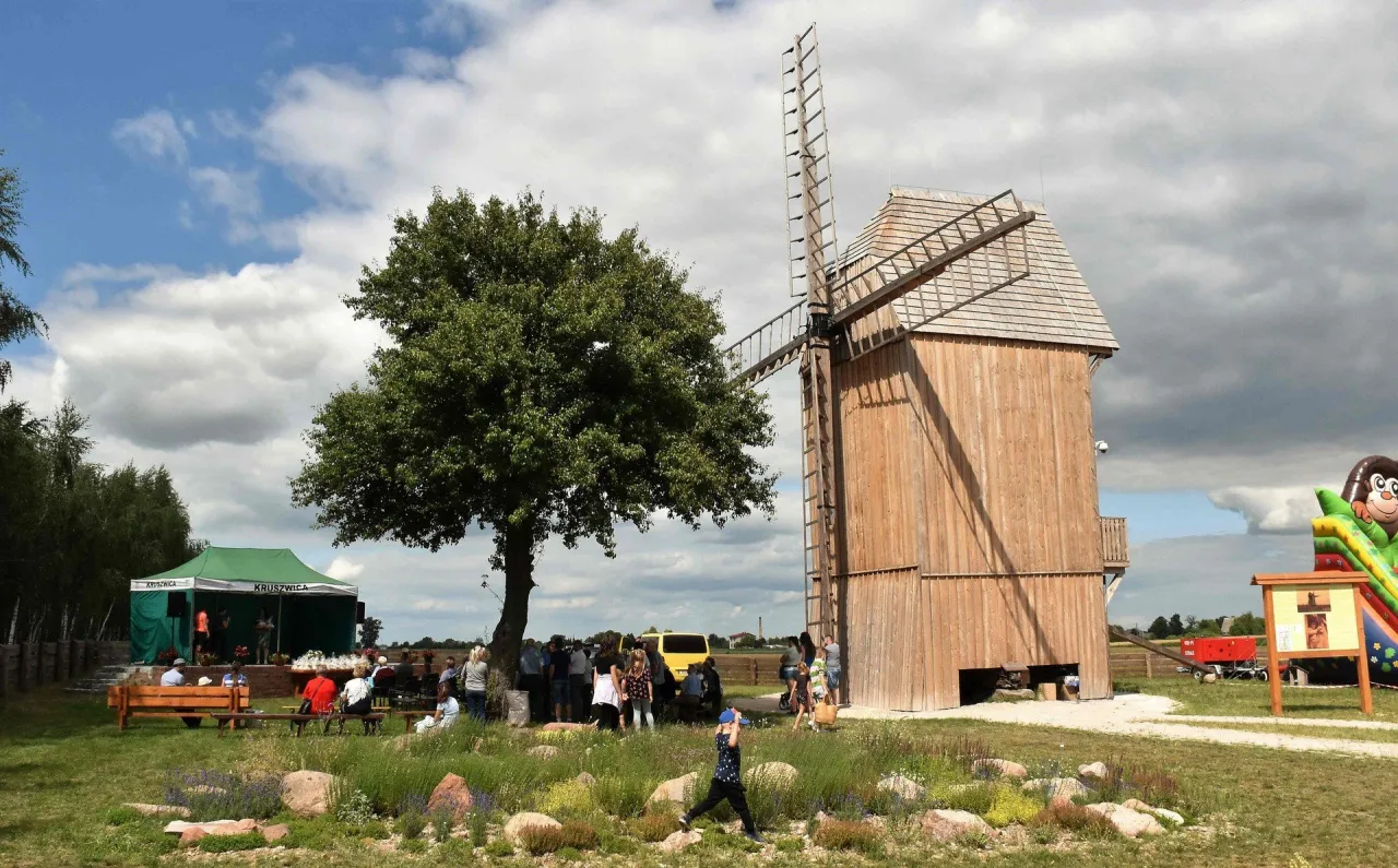 Drewniany wiatrak i zielony namiot z ludźmi, tworzą malowniczy krajobraz, jedno z najpiękniejszych miejsc Kujawsko-Pomorskiego.