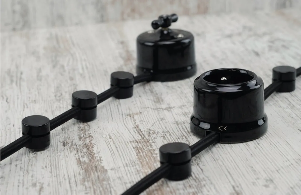 Elegancka instalacja natynkowa czarna z gniazdkiem i wyłącznikiem na drewnianym tle.