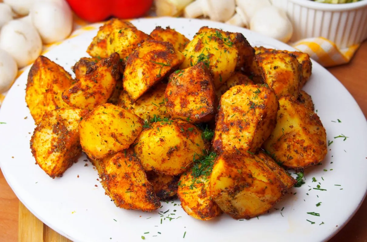 Złociste, pieczone ziemniaki z ziołami na białym talerzu. Czy pieczone ziemniaki są lekkostrawne? Tak, jeśli są dobrze przygotowane.