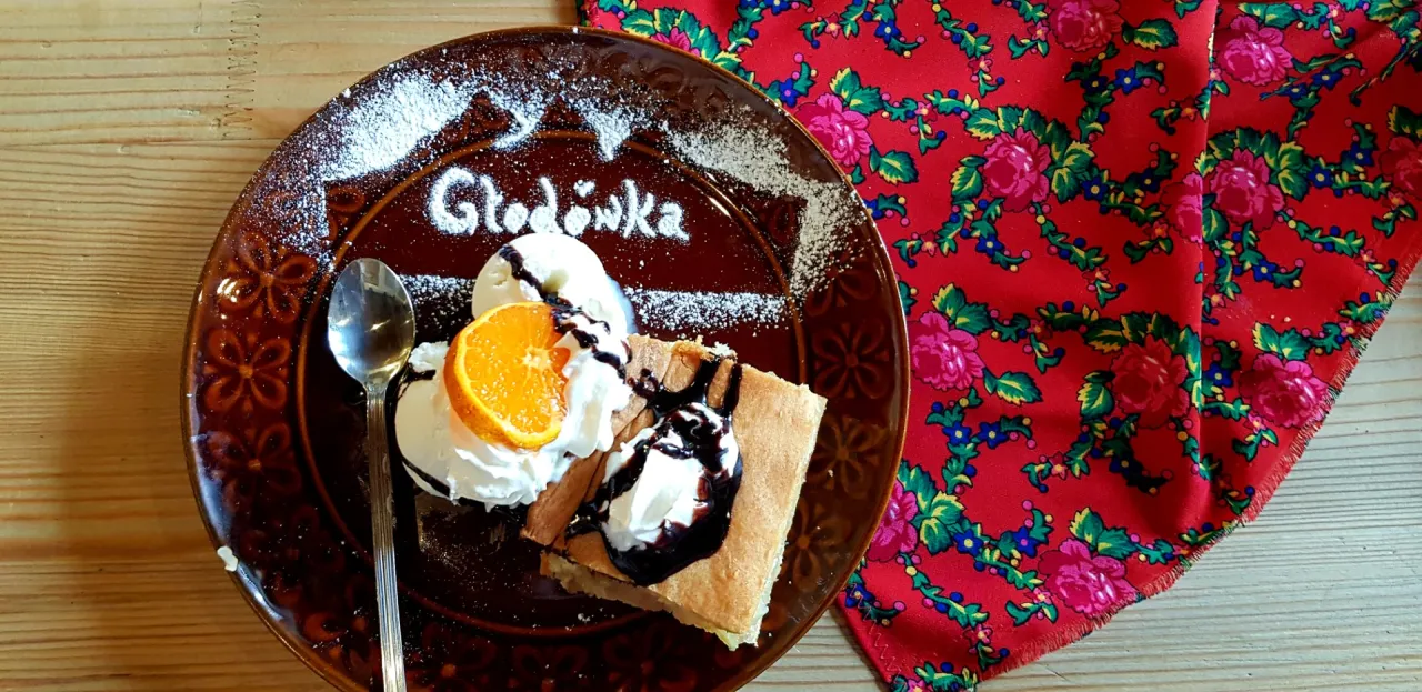 Słodka gościna na wierchu: ciasto, lody, pomarańcza i sos czekoladowy na talerzu z napisem 