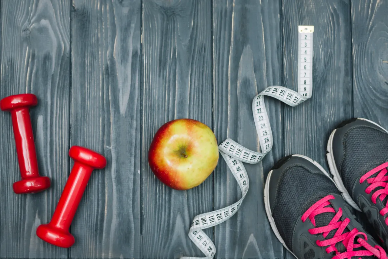 Dwa czerwone hantle, jabłko, miarka i buty sportowe. Zastanawiasz się, ile kalorii spala trening siłowy?