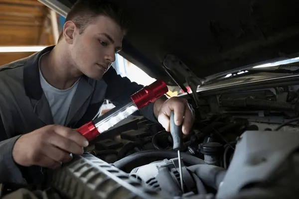m&eacute;canicien automobile inspectant un moteur avec une lampe torche