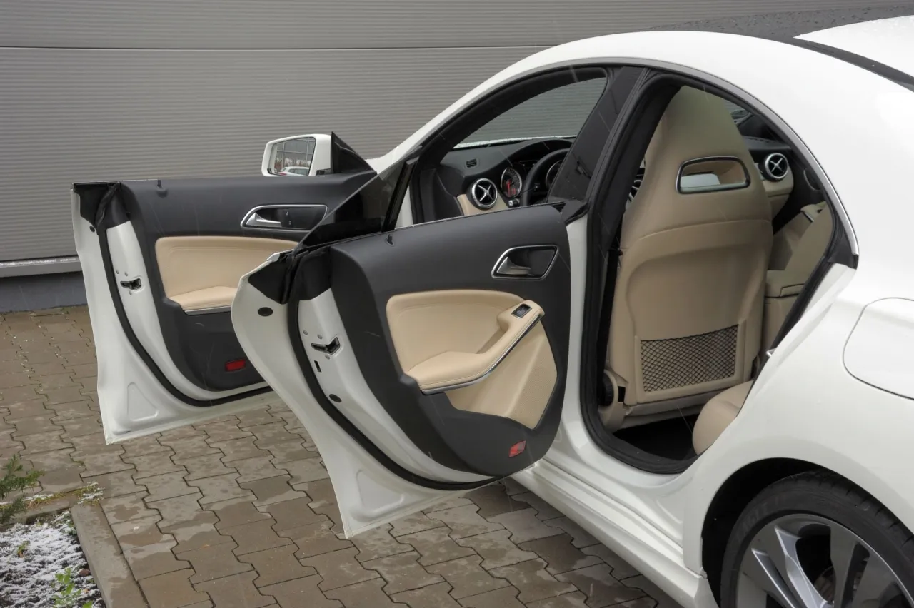 Wnętrze białego Mercedes CLA 45 AMG z otwartymi drzwiami, widoczne jasne fotele i panele drzwi.