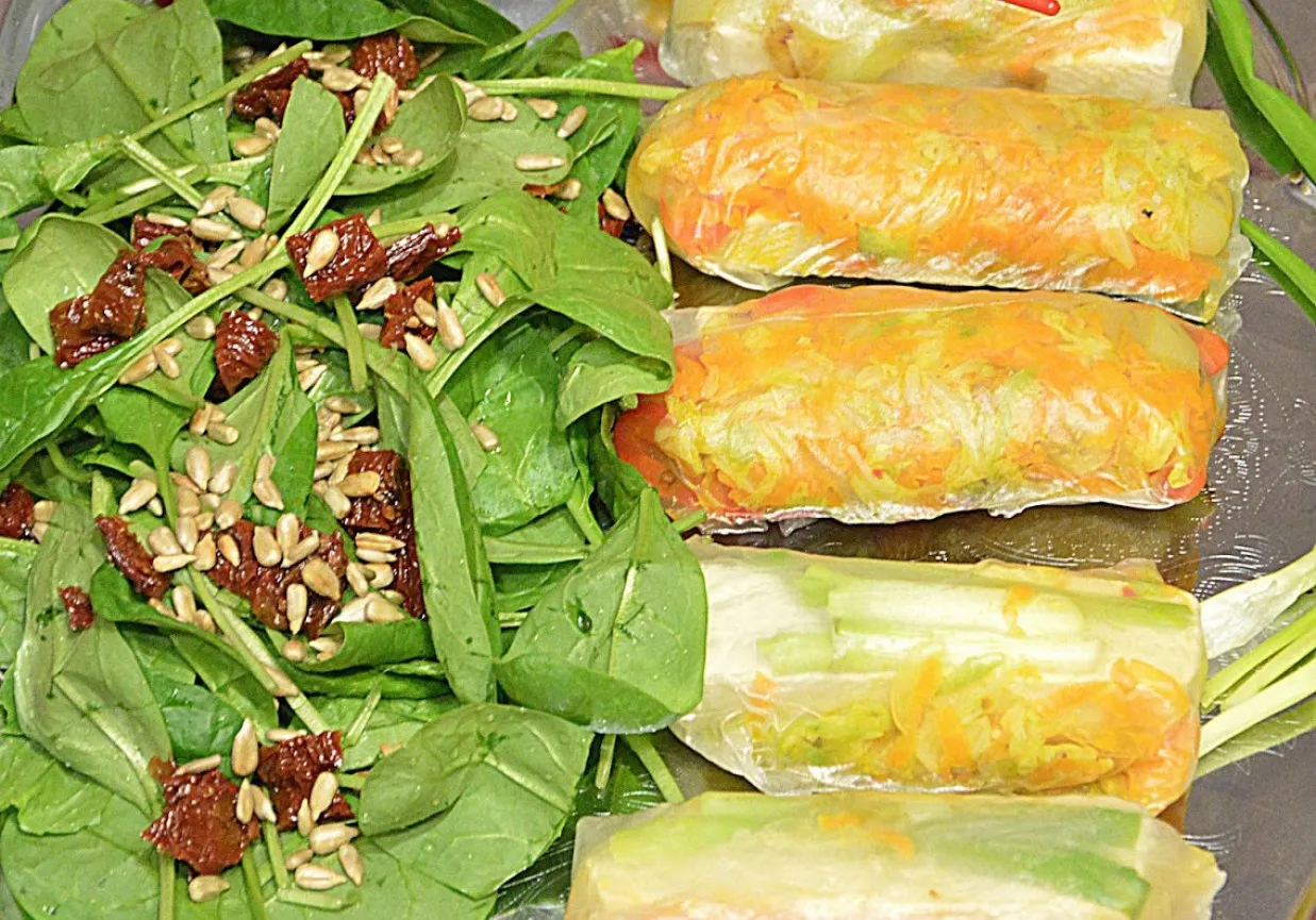 Świeży szpinak z suszonymi pomidorami i pestkami słonecznika obok gotowych sajgonek z warzywnym farszem.