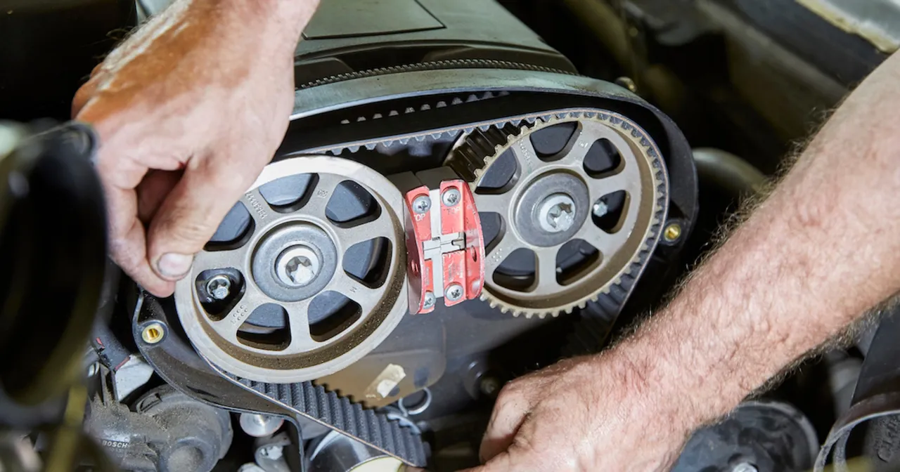 Mechanik pracuje przy silniku, wymieniając rozrząd w aucie. Widoczne koła zębate i pasek rozrządu.