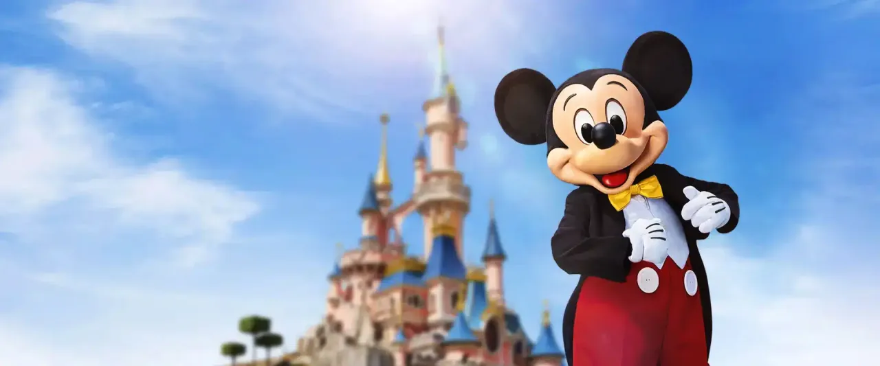 Myszka Miki wita gości w Disneylandzie w Paryżu, na tle bajkowego zamku.