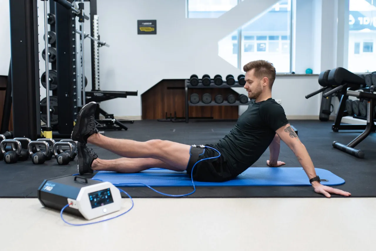 Mężczyzna ćwiczy na macie z urządzeniem do rehabilitacji. To miejsce, gdzie najszybciej na rehabilitacje wr&oacute;cisz do formy.