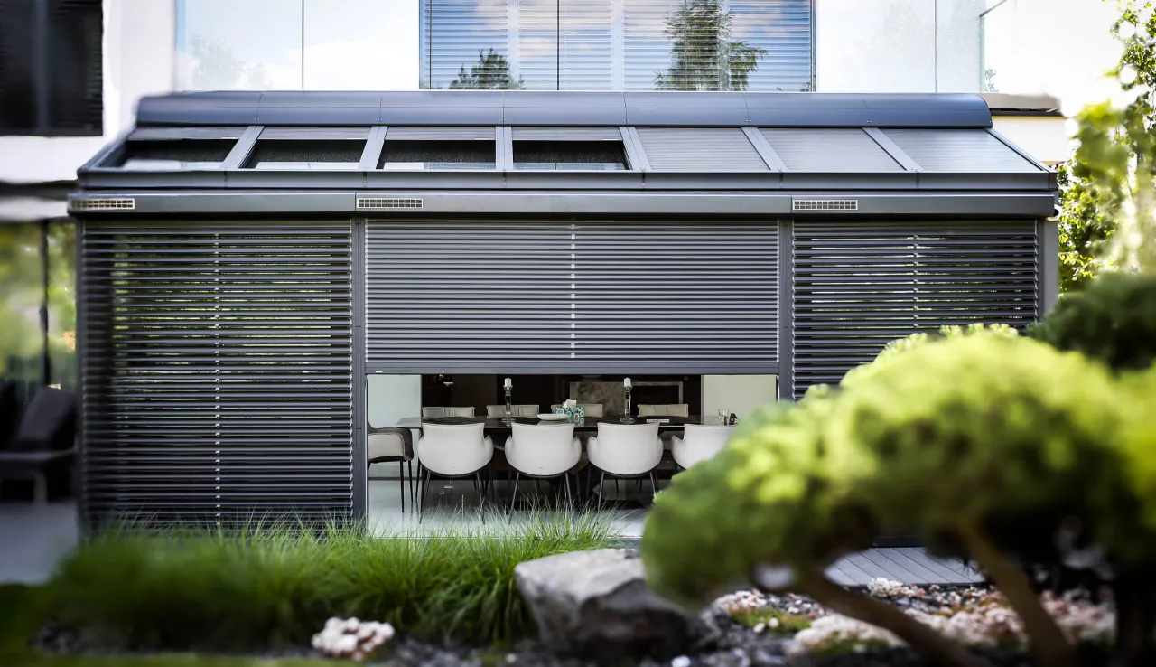 Nowoczesna bryła domu z wysuwanymi roletami fasadowymi zewnętrznymi, chroniącymi wnętrze z jadalnią.