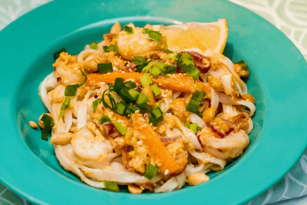 Pyszny makaron ryżowy z sosem, krewetkami, marchewką i orzeszkami ziemnymi, posypany szczypiorkiem.