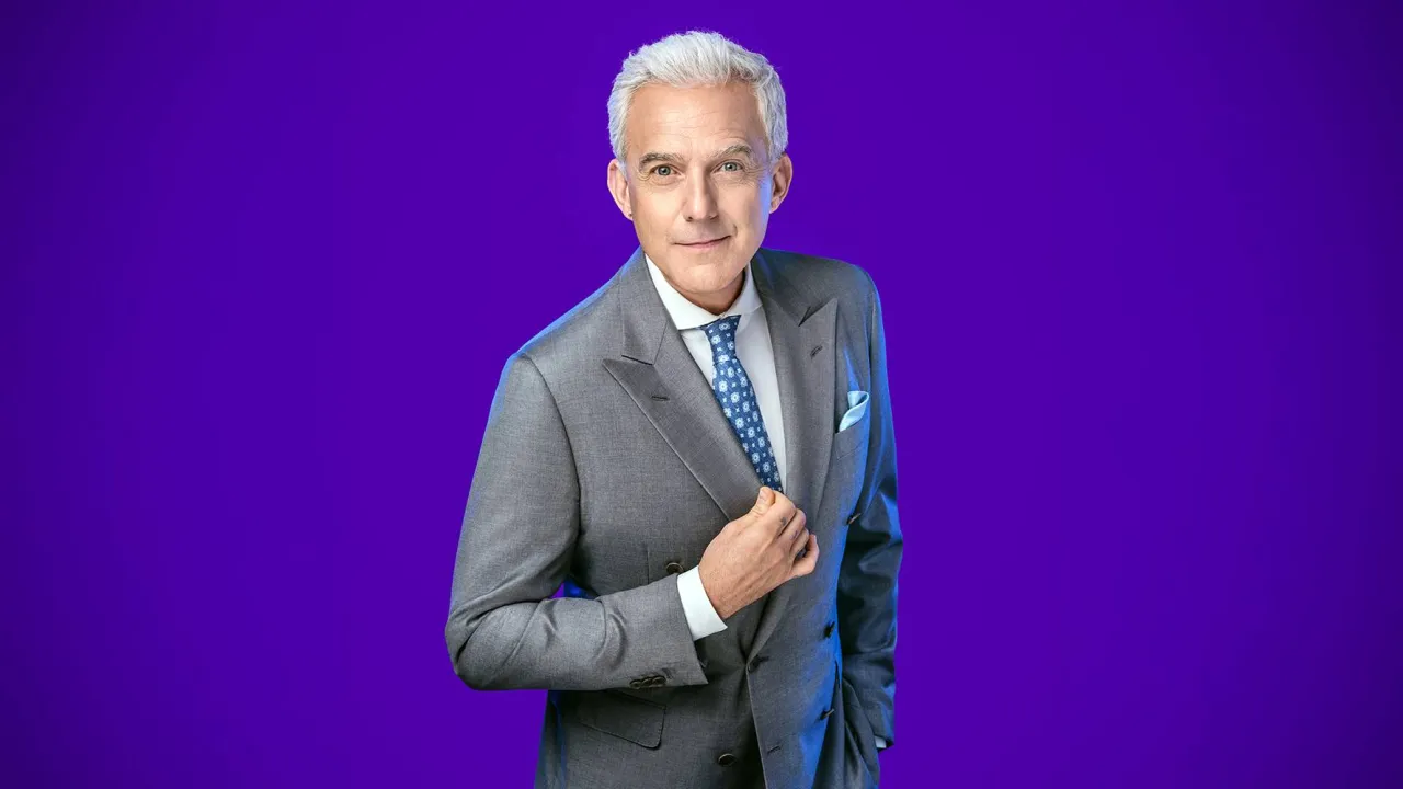 Hubert Urbański w szarym garniturze, gotowy do prowadzenia programu 