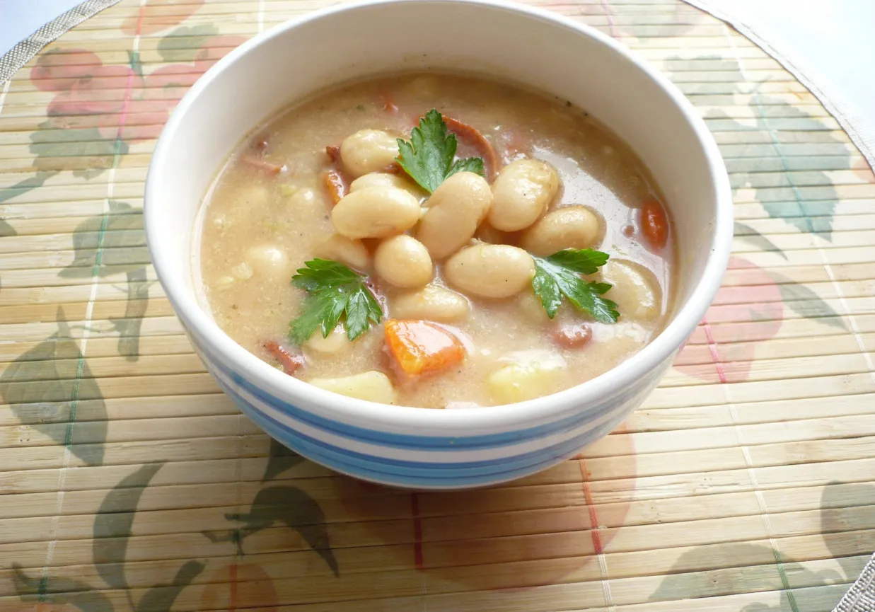Gęsta zupa fasolowa z kawałkami kiełbasy i marchewki. Idealna na chłodne dni, a do zupy fasolowej warto dodać świeżą natkę pietruszki.
