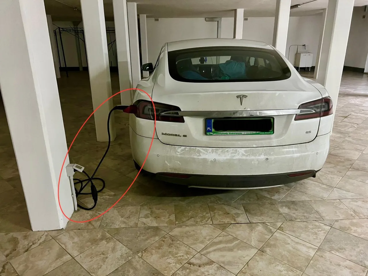 Biały Tesla Model S ładuje się w garażu. Zastanawiasz się, ile trwa ładowanie samochodu elektrycznego w domu? To zależy od mocy ładowarki.