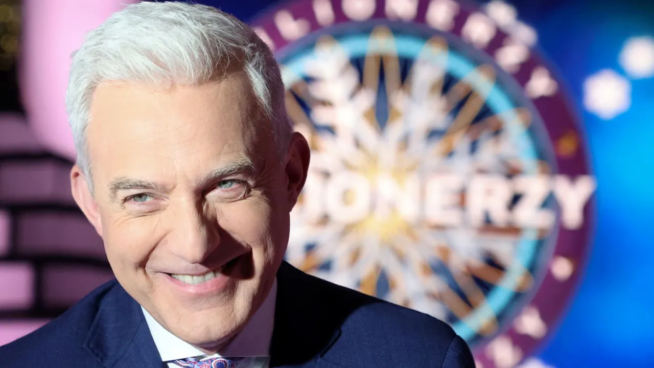 Uśmiechnięty Hubert Urbański w garniturze, w tle koło z napisem 