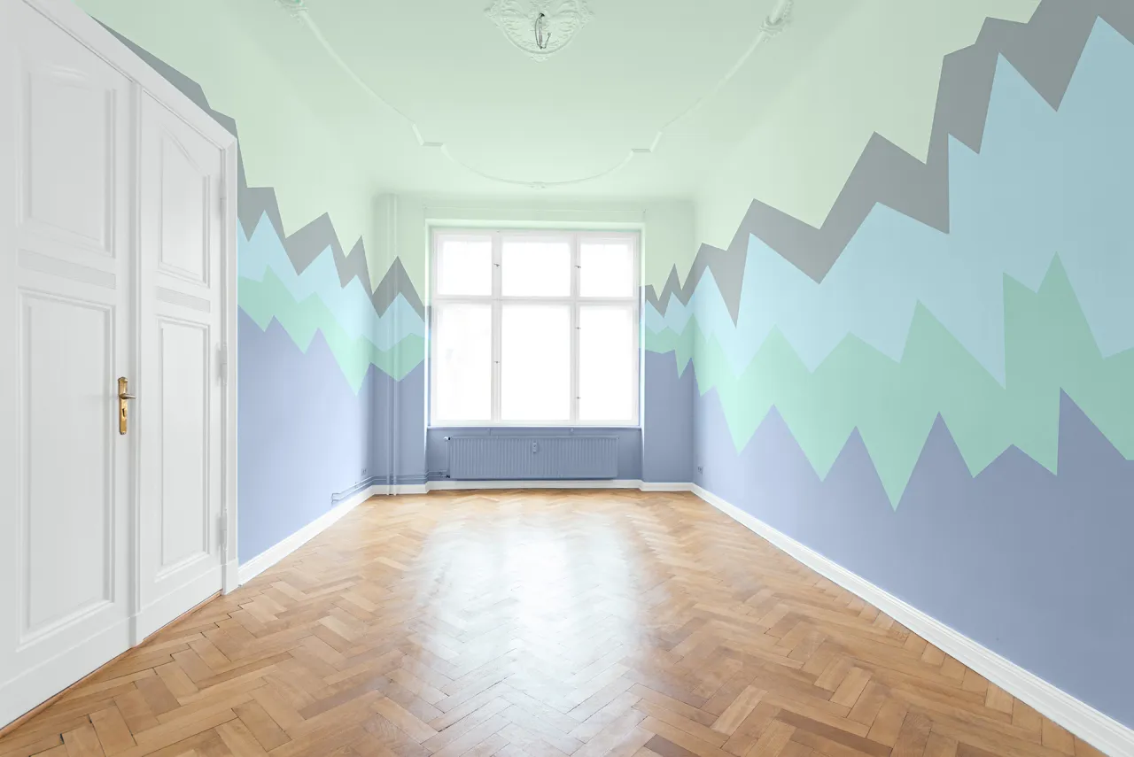 Pokój z geometrycznym wzorem na ścianach w odcieniach niebieskiego i zieleni. Czy malować sufit w kolorze ścian? Jasny sufit i białe drzwi kontrastują z kolorowymi ścianami.