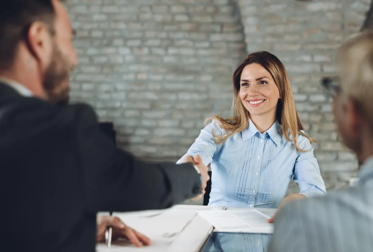 Uśmiechnięta kobieta podaje rękę szefowi, omawiając jak napisać podanie o podwyżkę.