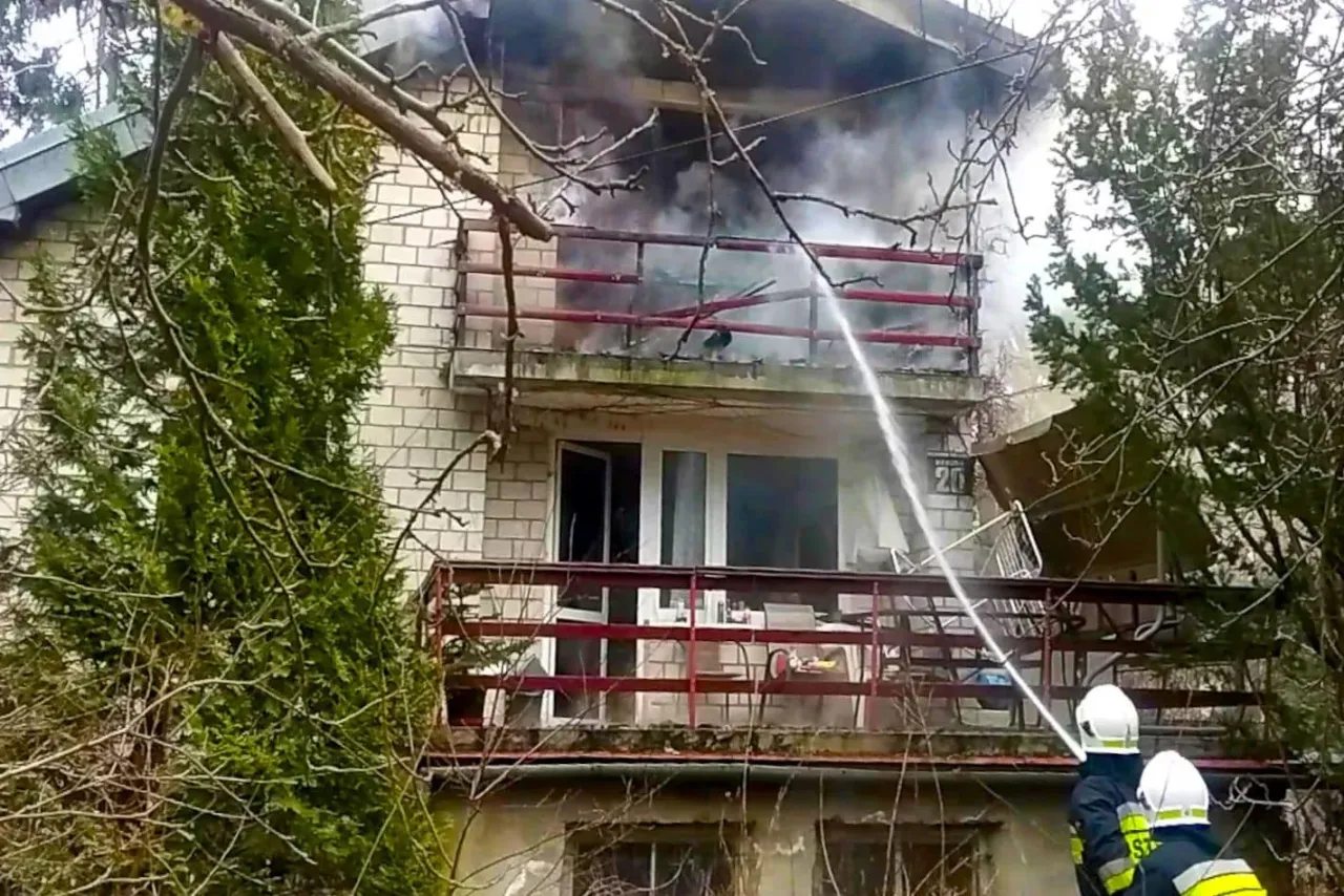 Strażacy gaszą pożar na balkonie, trwa wycena szkody po pożarze. Dym unosi się z budynku.