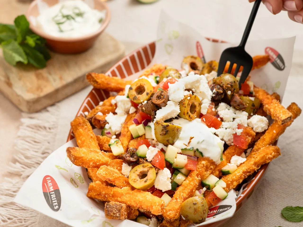 Chrupiące frytki z czymś pysznym: oliwkami, fetą, pomidorami i og&oacute;rkiem, polane jogurtowym sosem.