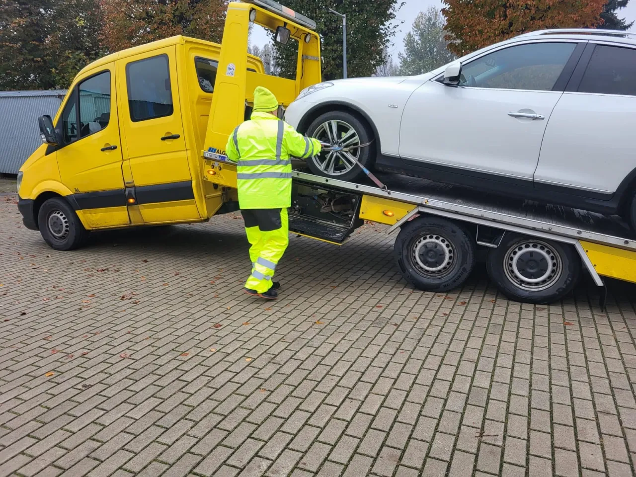 Pomoc drogowa ładuje biały samochód na lawetę. Czy można holować samochód na drodze ekspresowej? Tak, ale tylko w określonych warunkach.