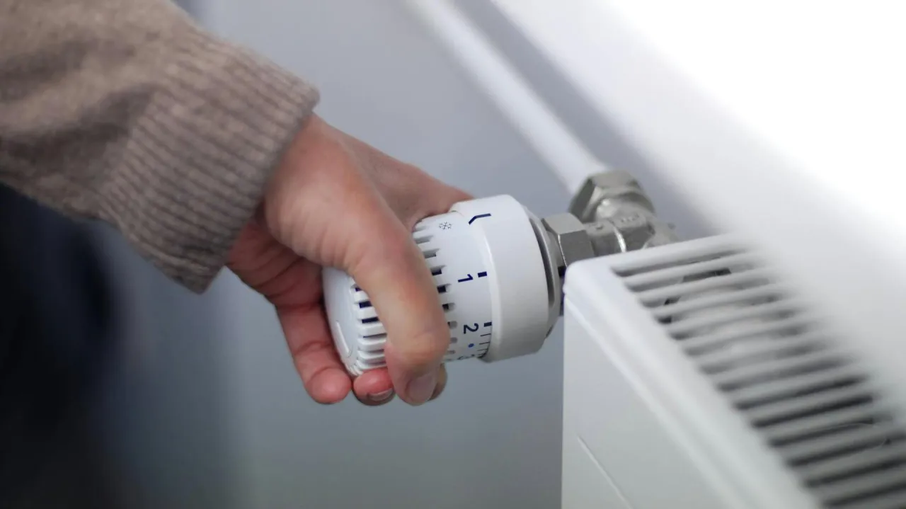Dłoń reguluje termostat grzejnika, zastanawiając się, czy zakręcać grzejniki na noc.