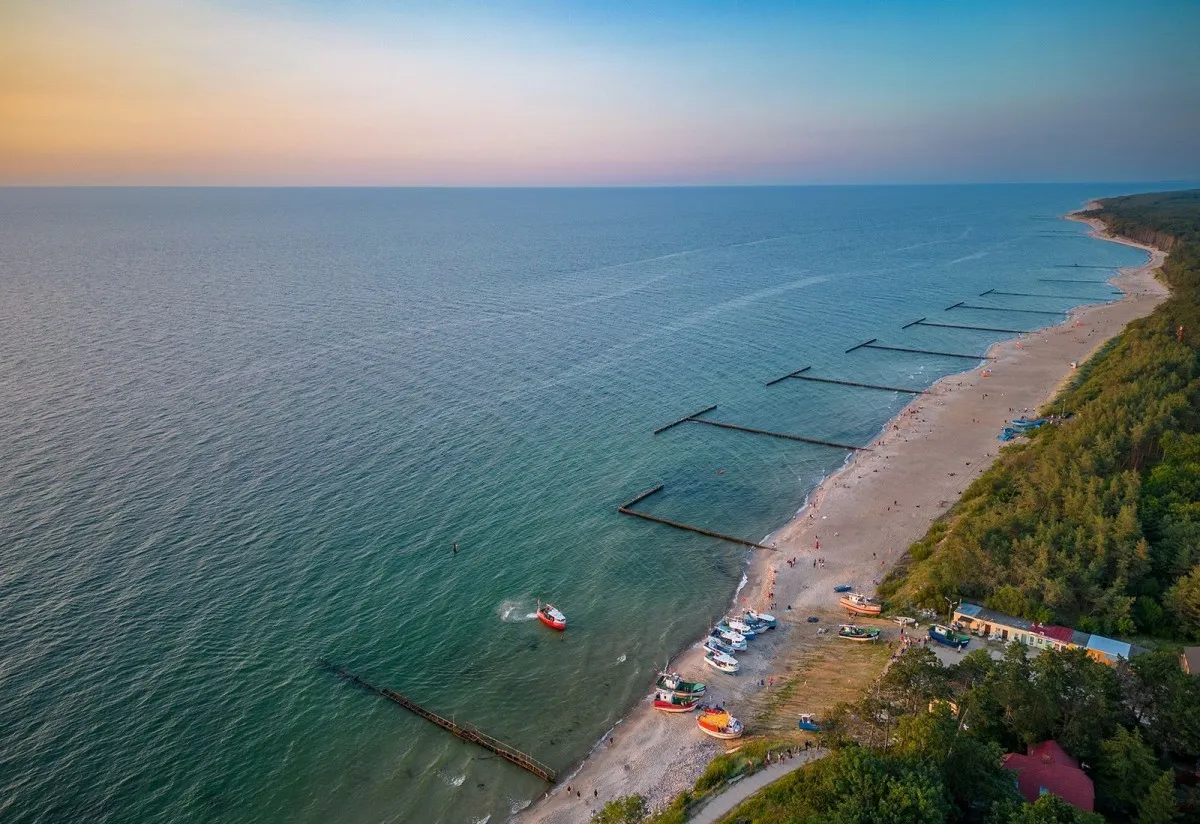 Piękna plaża i morze, gdzie jest Jarosławiec? Widać łodzie, falochrony i las.