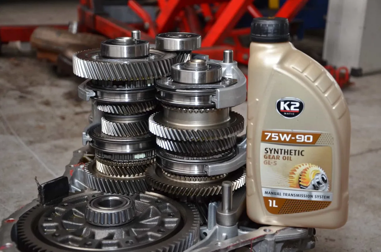 Zestaw k&oacute;ł zębatych skrzyni bieg&oacute;w w samochodzie, obok butelka oleju 75W-90.