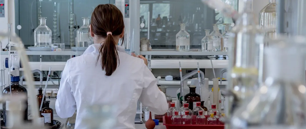 Naukowczyni w białym fartuchu pracuje w laboratorium, przygotowując się do otwarcia laboratorium diagnostycznego. W tle szkło laboratoryjne i sprzęt.