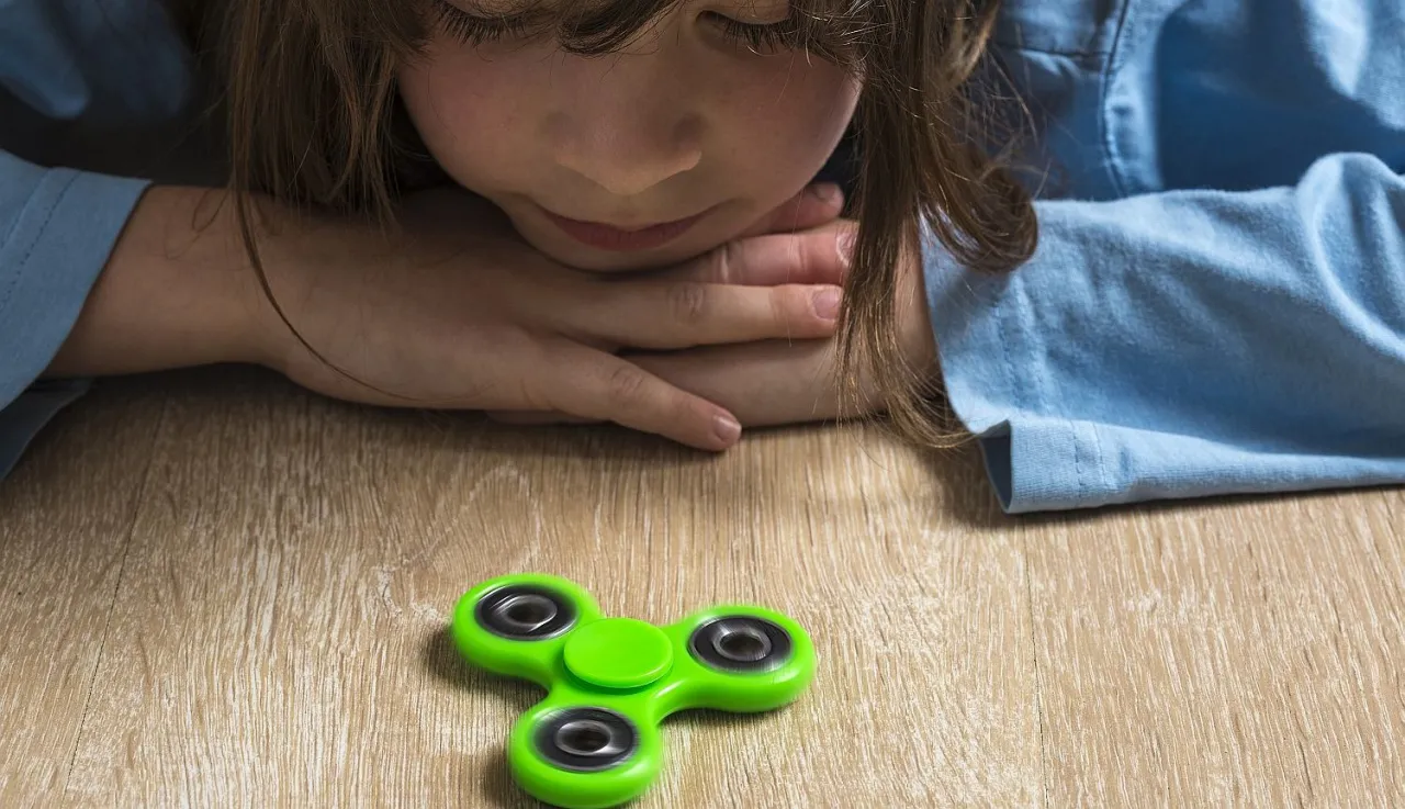 Dziecko z zaciekawieniem obserwuje zielony spinner dla dzieci wirujący na drewnianym blacie.