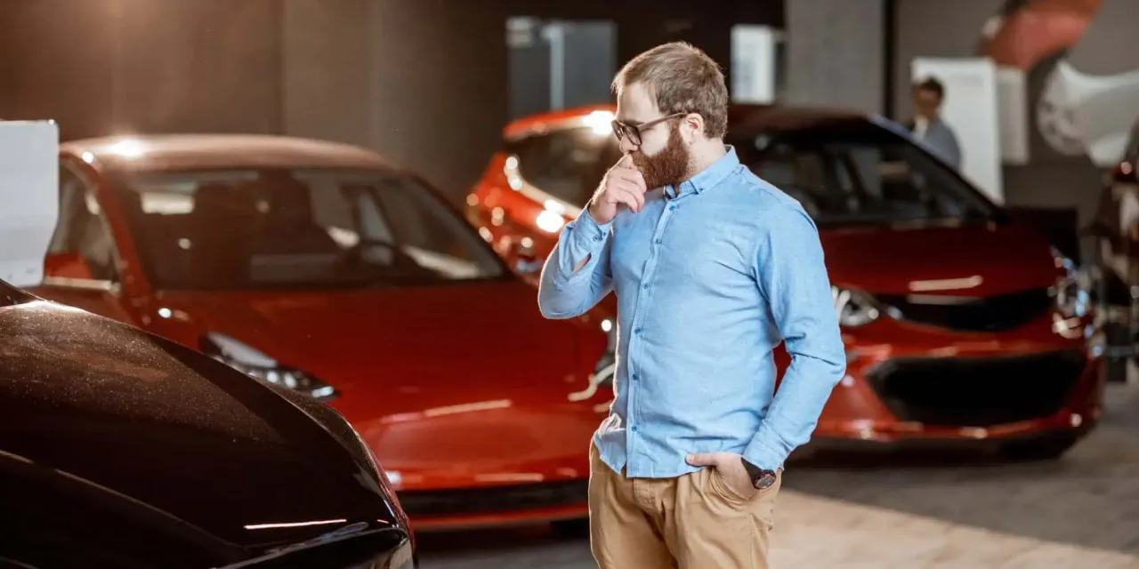 Mężczyzna w okularach zastanawia się nad wyborem samochodu na rynku motoryzacyjnym.