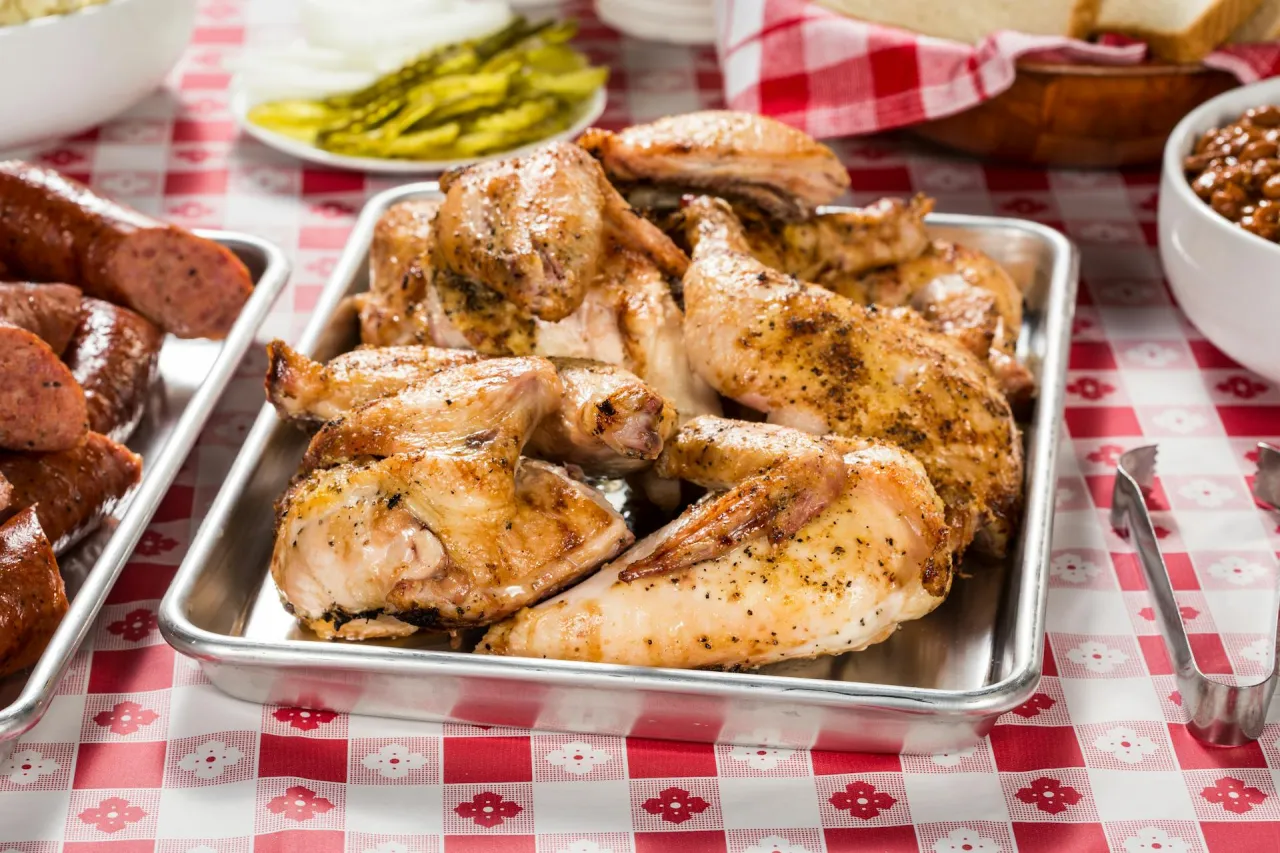 Pyszny, pieczony kurczak na tacy, obok kiełbasek i fasolki. Zastanawiasz się, ile białka ma kurczak? To świetne źr&oacute;dło!