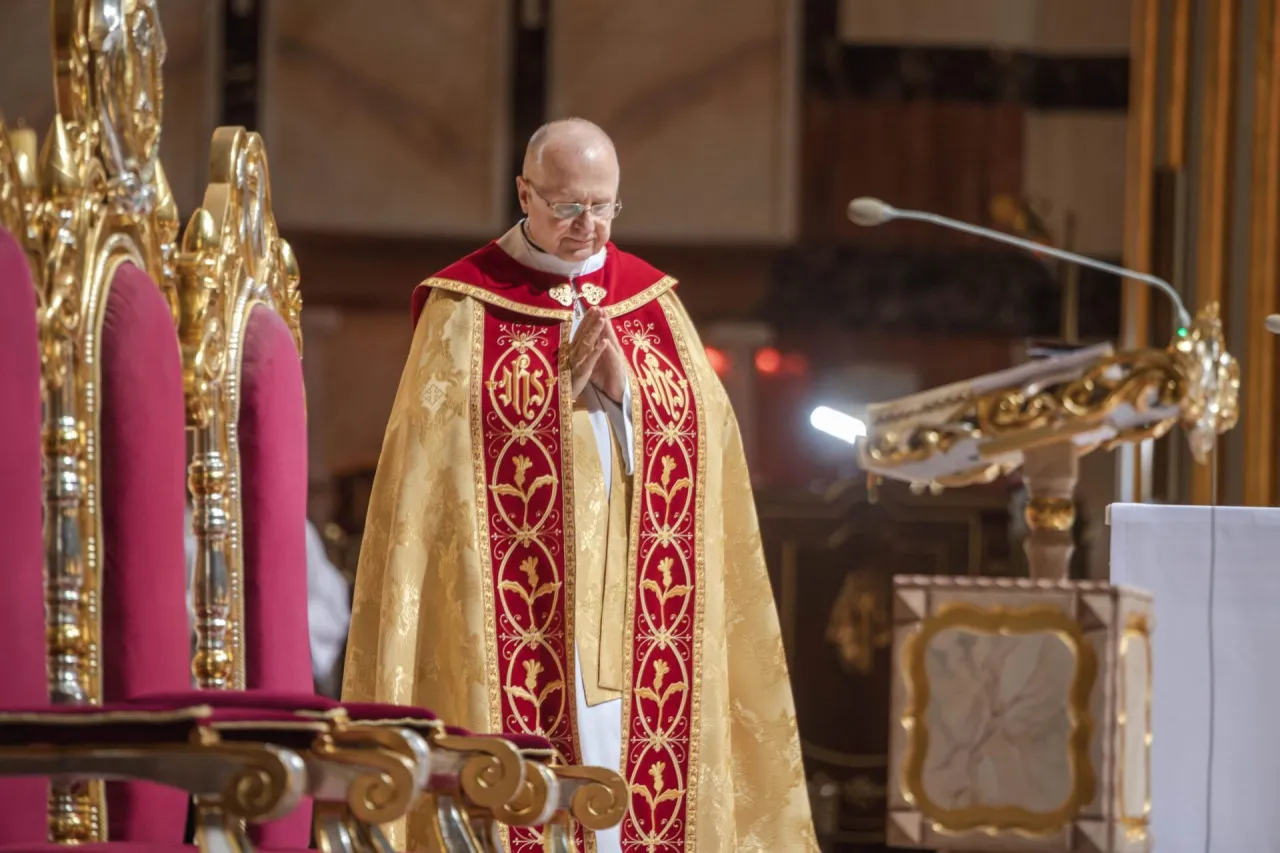 Kapłan w złotej kapie z czerwonymi zdobieniami modli się, prowadząc nieszpory za zmarłego.