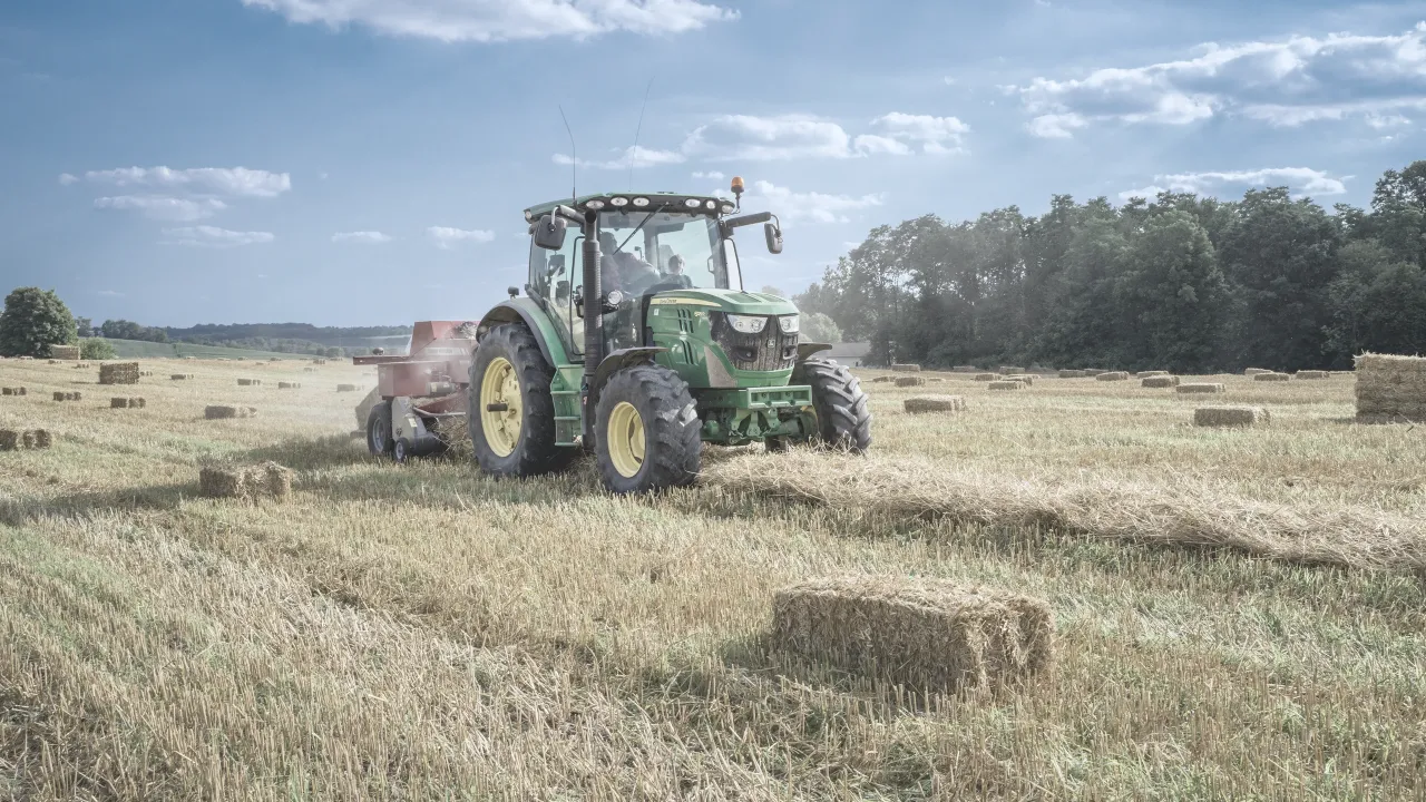 Zielony traktor prasuje słomę na polu. Nowy właściciel ziemi rolnej, nie rolnik, uczy się jej obsługi.