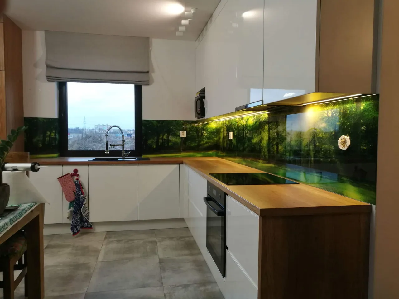 kuchnia z białymi meblami drewnianym blatem i szklaną ścianą lacobel