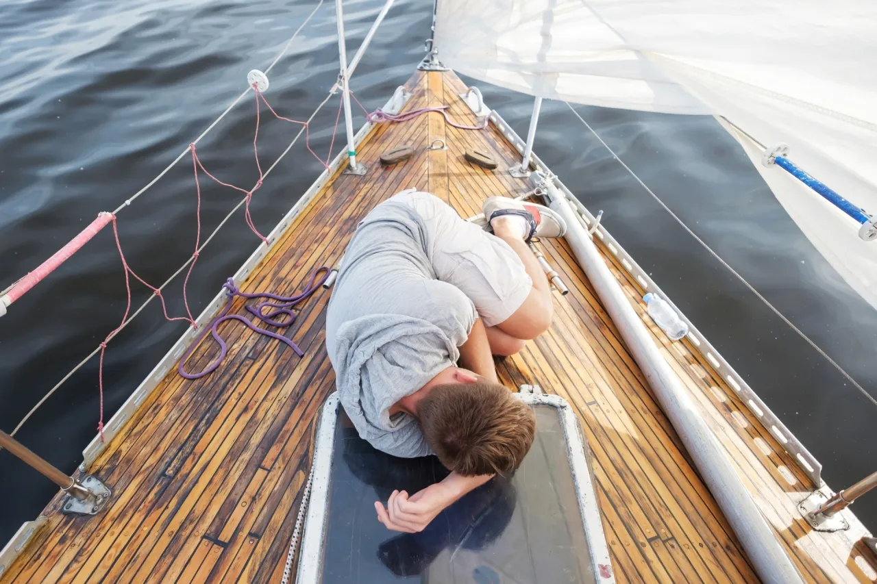 Choroba morska podczas rejsu na Wyspy Kanaryjskie. Młody mężczyzna skulony na pokładzie jachtu, cierpiący na mdłości.