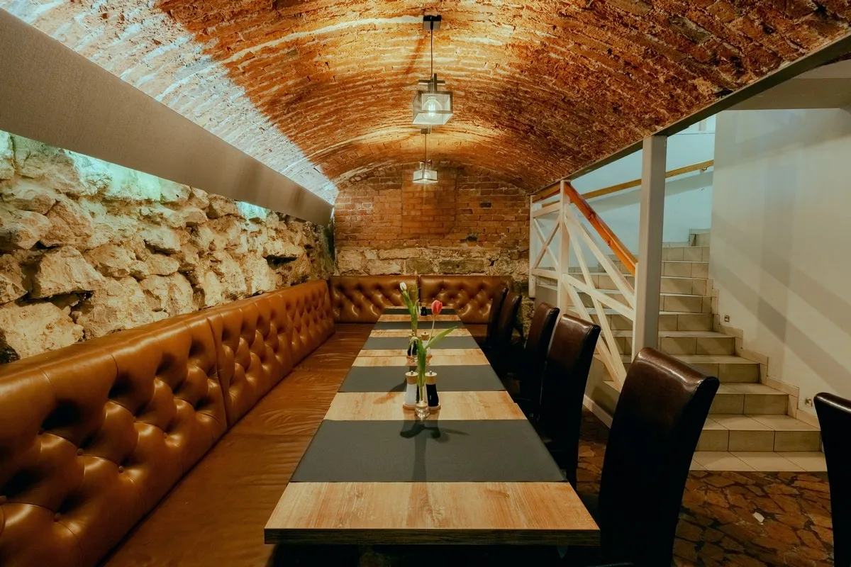 Przytulne wnętrze restauracji z ceglanym sufitem i kamienną ścianą. Idealne miejsce, gdzie na obiad w Krakowie.