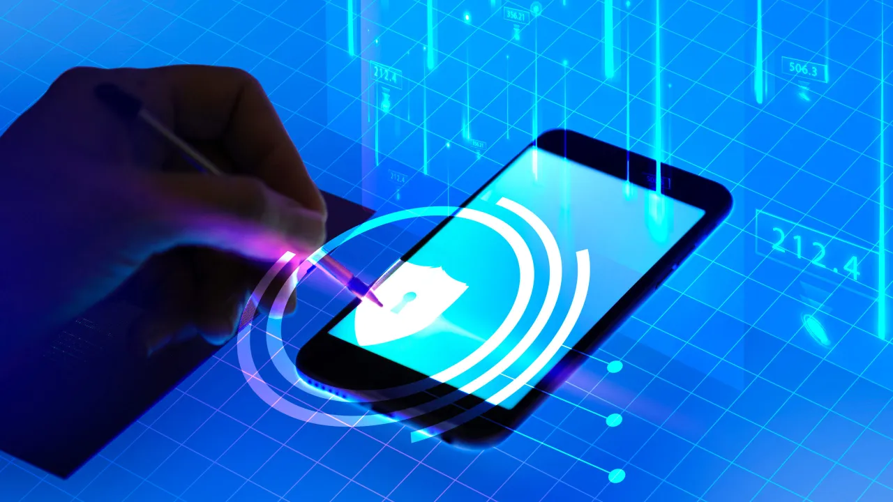 Dłoń pisze na ekranie smartfona z ikoną tarczy i kł&oacute;dki, symbolizującą bezpieczeństwo i token CSRF.