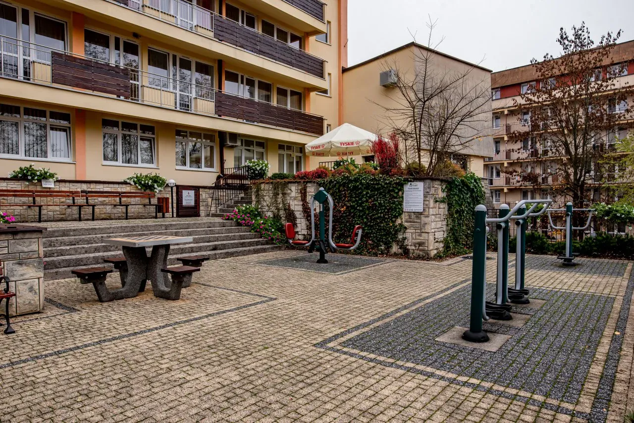 Sanatorium Leśnik Drzewiarz Krynica Zdrój, ul. Podgórna 1. Siłownia plenerowa i stolik do gry w szachy przed budynkiem.
