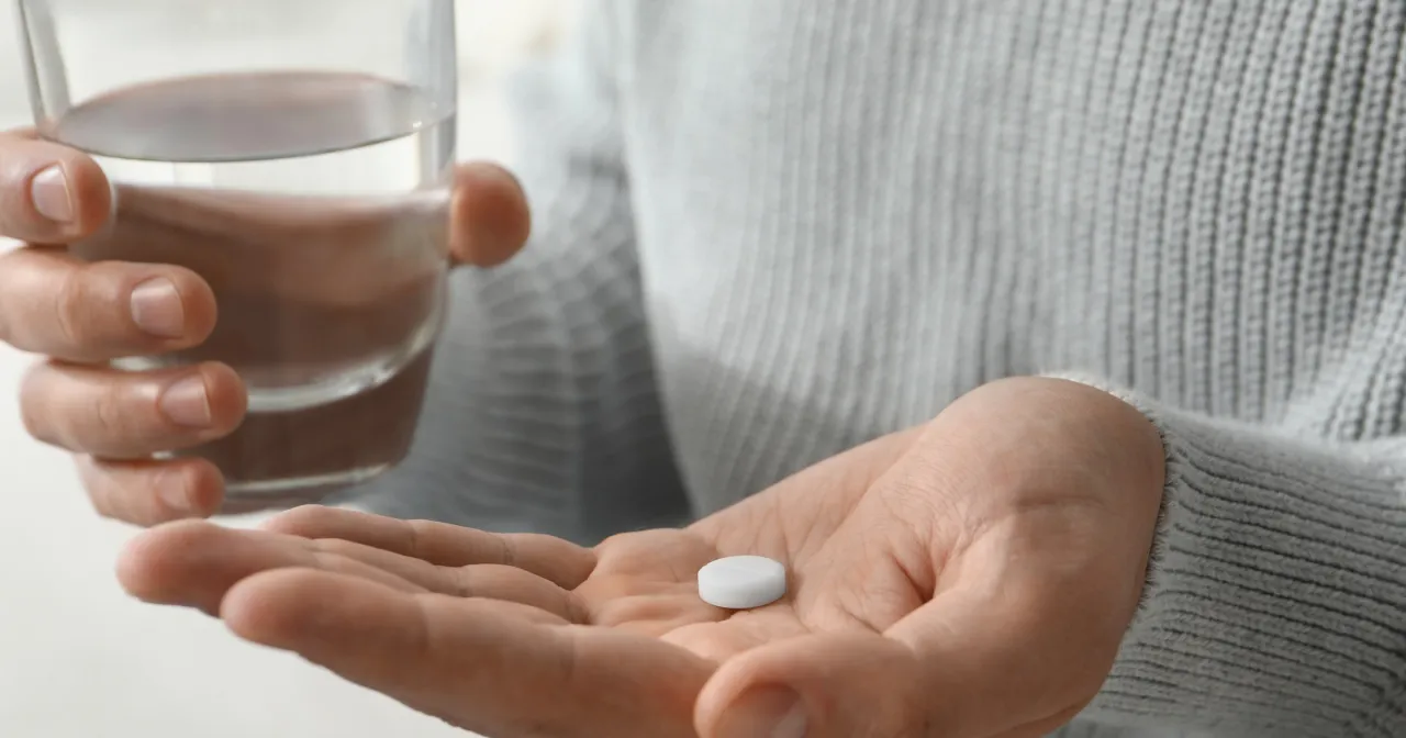 Dłoń trzyma białą tabletkę i szklankę wody. Przed przyjęciem suplementu, sprawdź l-glutamina przeciwwskazania.