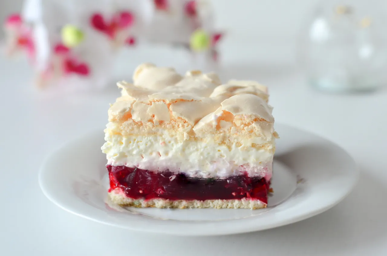 Malinowa rozkosz bez pieczenia: warstwy biszkoptu, kremu, galaretki malinowej i bezy. Pyszny deser na talerzyku.