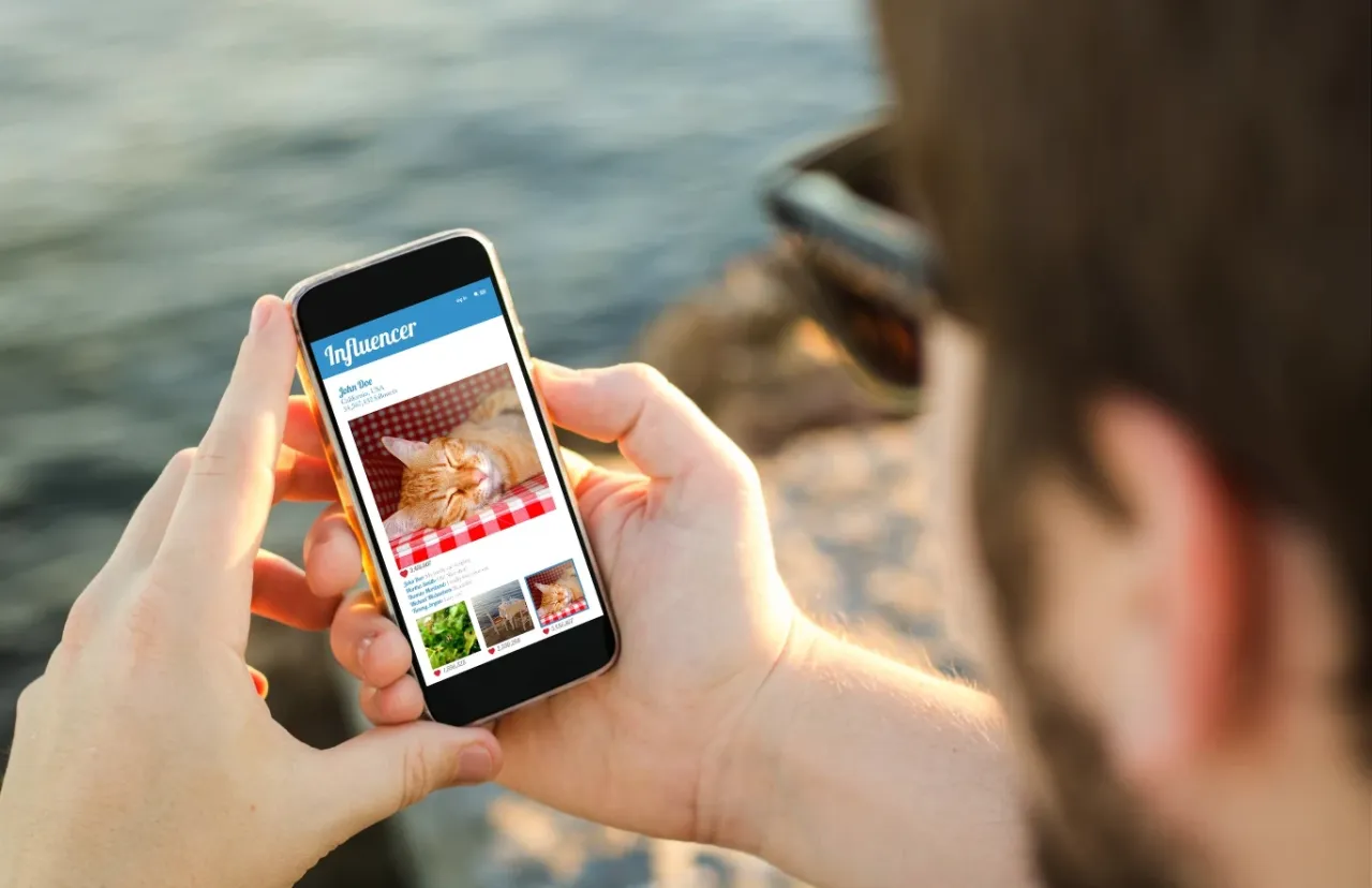 Osoba przegląda profil influencera na telefonie. Czy influencerzy promujący szybkie pożyczki z nagrodami sami z nich korzystają?