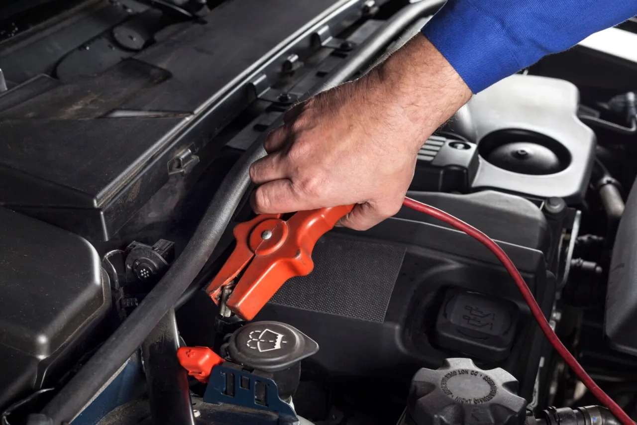 Ręka podłącza klemę do akumulatora, pokazując jak odpalić Toyotę hybrydę na kable.