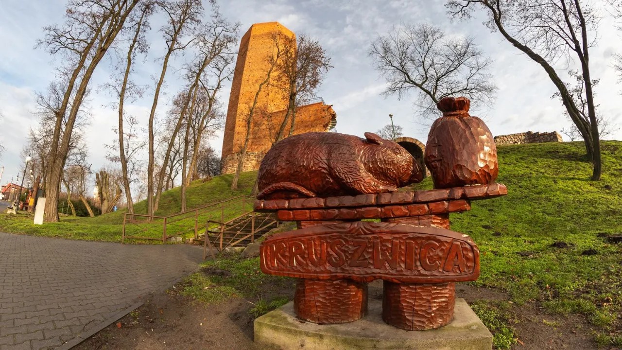 Drewniane rzeźby z Kruszwicy, nawiązujące do legendy o Popielu i myszach, na tle wieży.