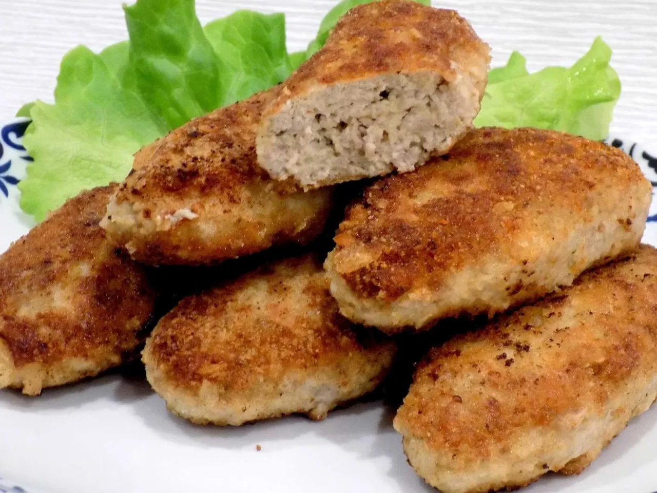 Złociste kotlety mielone wieprzowe lub drobiowe, jeden przekrojony, na talerzu z sałatą.